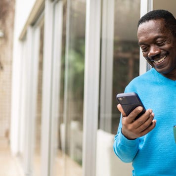 Senior man holding coffee/tea mug and using smartphone at home