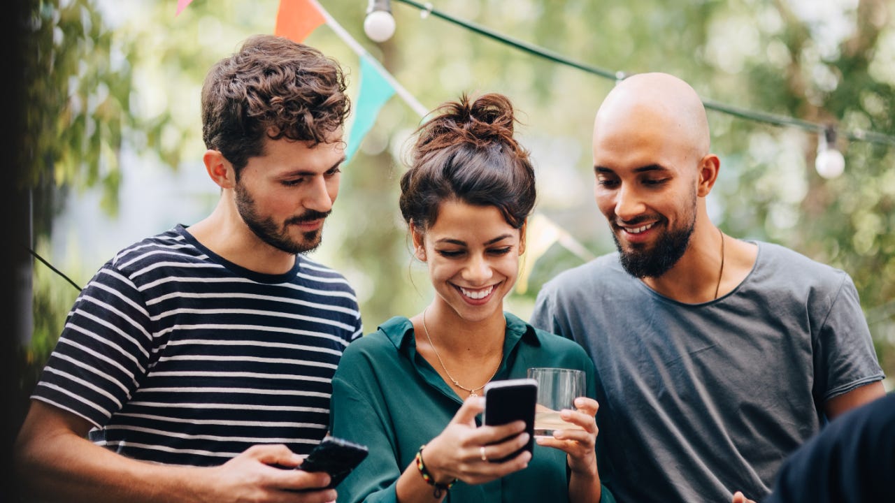 A group of smiling millennials looks at a phone