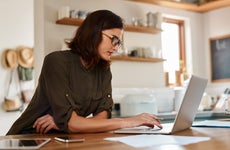 Adult woman with glasses focuses intently on her laptop screen in a kitchen