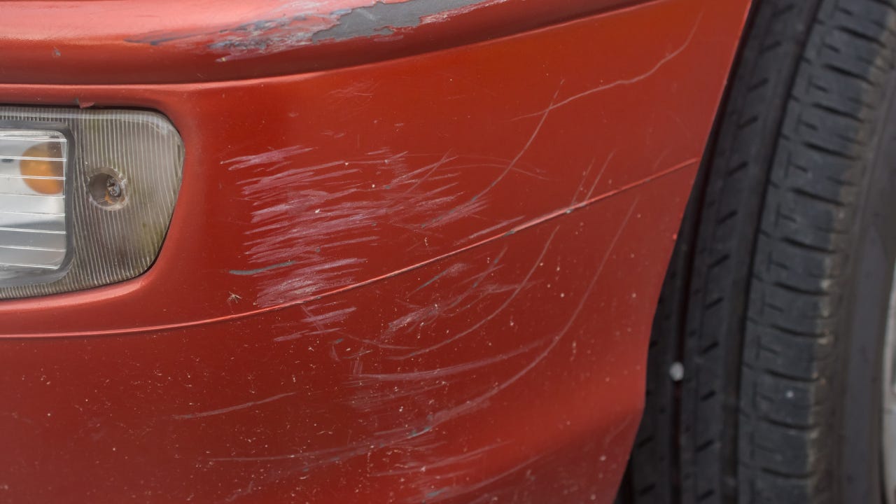 Red bumper car scratched with deep damage to the paint.