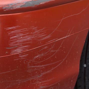 Red bumper car scratched with deep damage to the paint.