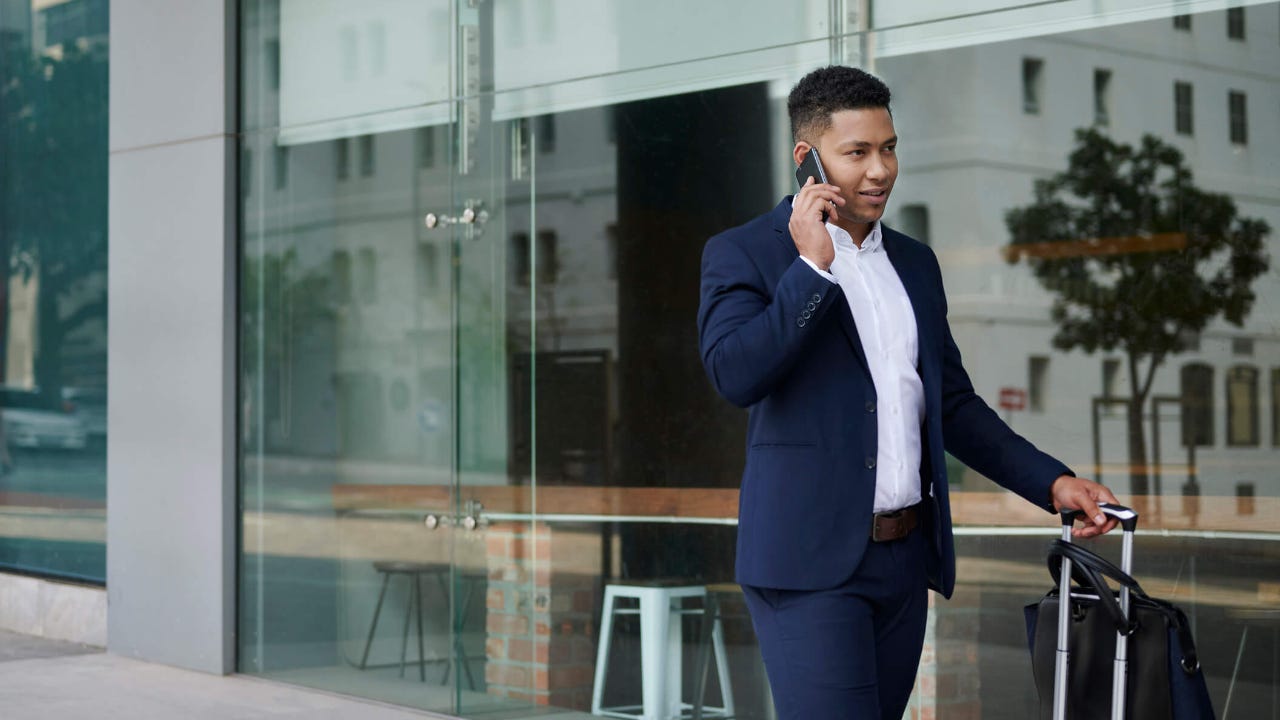 Smiling businessman with a suitcase talking on his phone outside of an office