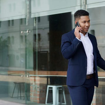 Smiling businessman with a suitcase talking on his phone outside of an office