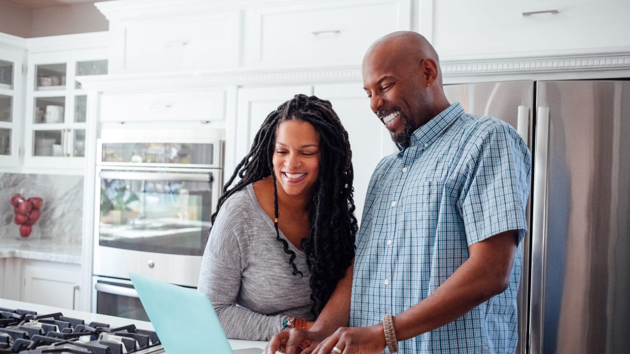 Man and woman using laptop in kitchen at home