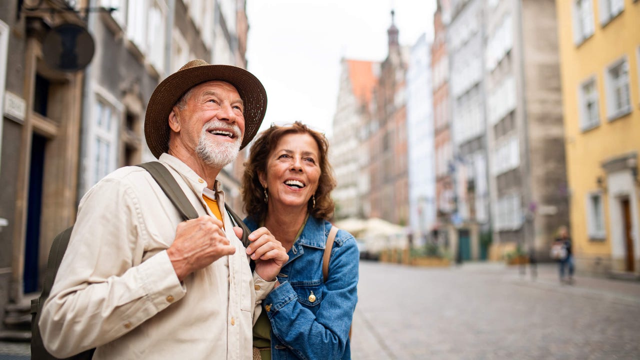 Portrait of happy senior couple tourists outdoors in historic town