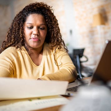 Black adult reviewing tax forms at their desk with an open laptop nearby.