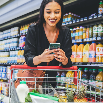 Shot of a young woman using a smartphone while shopping in a grocery store