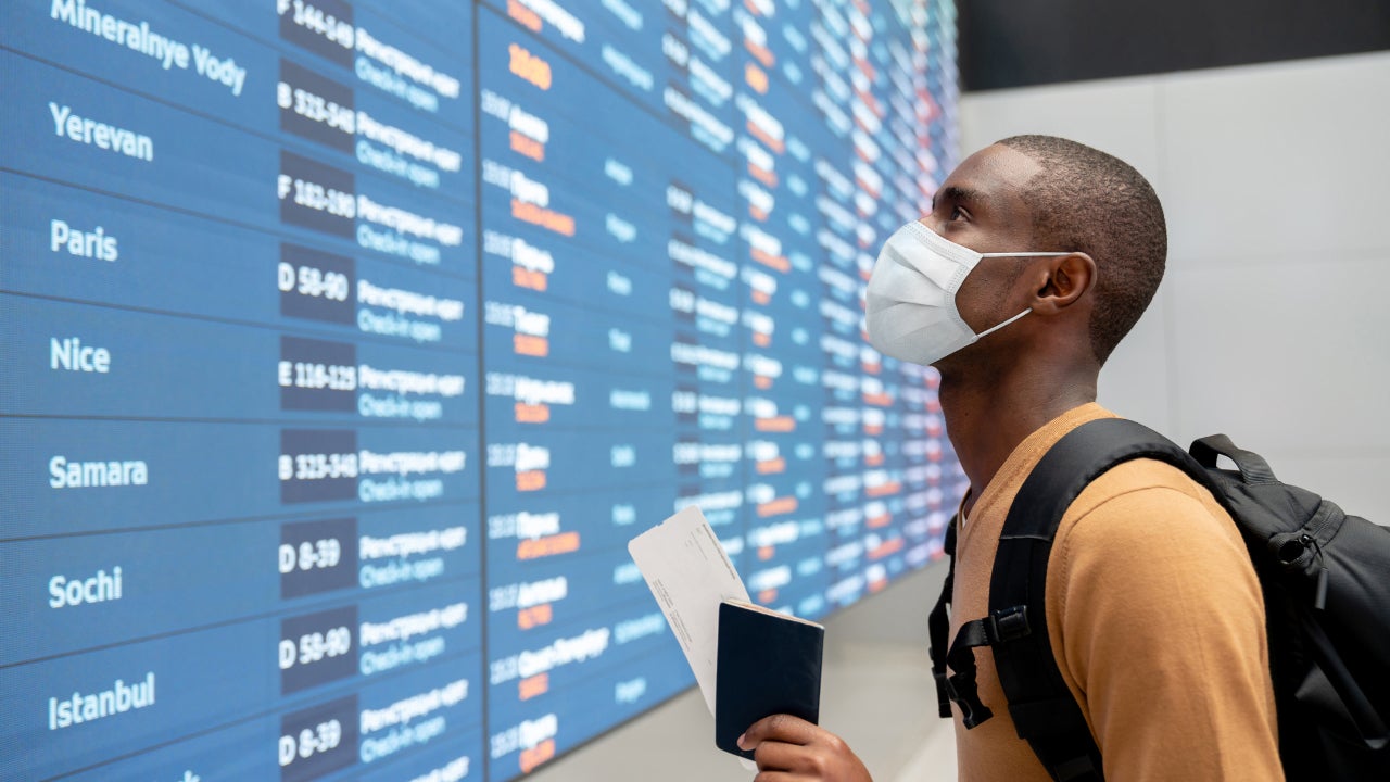 Masked main in airport looking at flight times