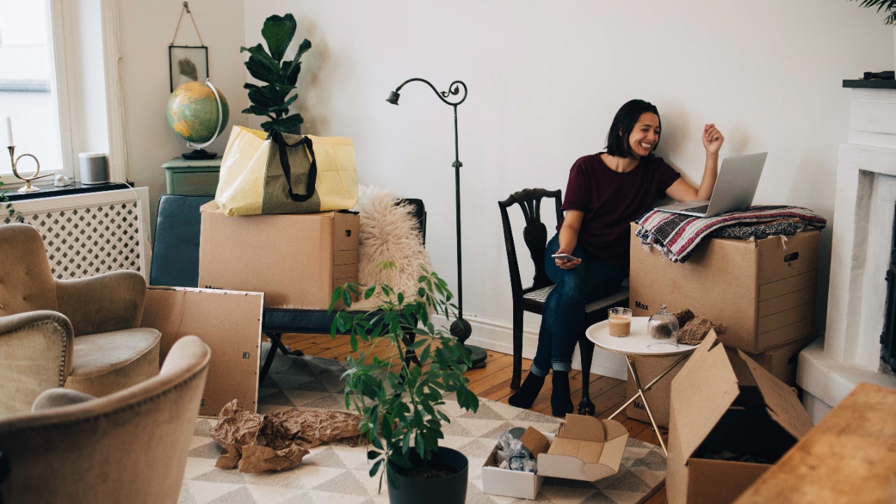 Smiling woman looking at laptop surrounded by boxes