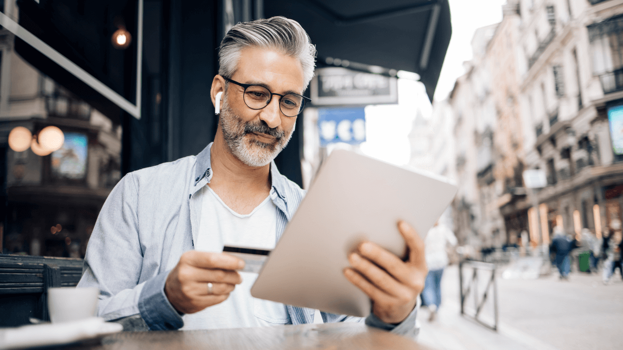 Man looking at credit card and tablet at outdoor cafe