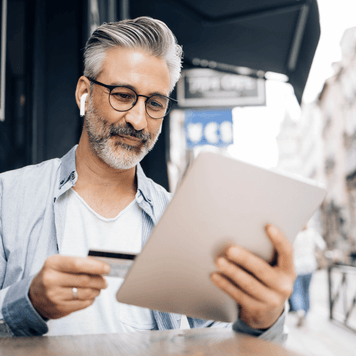 Man looking at credit card and tablet at outdoor cafe