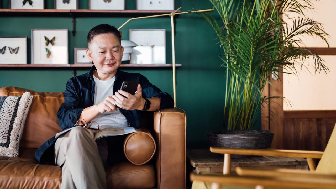 Senior man using smartphone while relaxing on the sofa in the living room at home