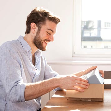 Young man sitting at a table unpacking cardboard box