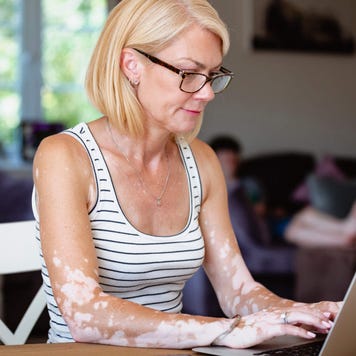 Blonde woman sitting her dining table at home with a laptop open in front of her