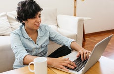 Woman sitting on floor and working on laptop. Female sitting at table with cup of coffee and using laptop.