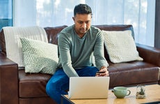man sitting on the couch while working on laptop and holding credit card