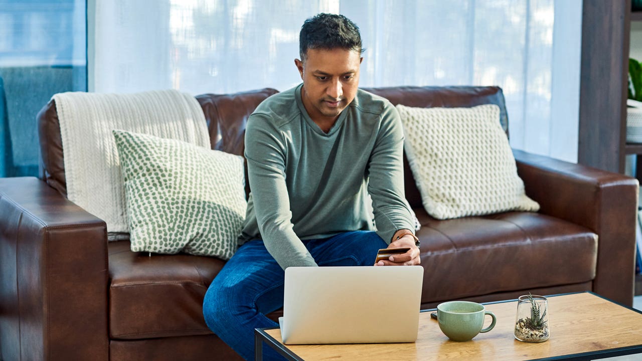 man sitting on the couch while working on laptop and holding credit card