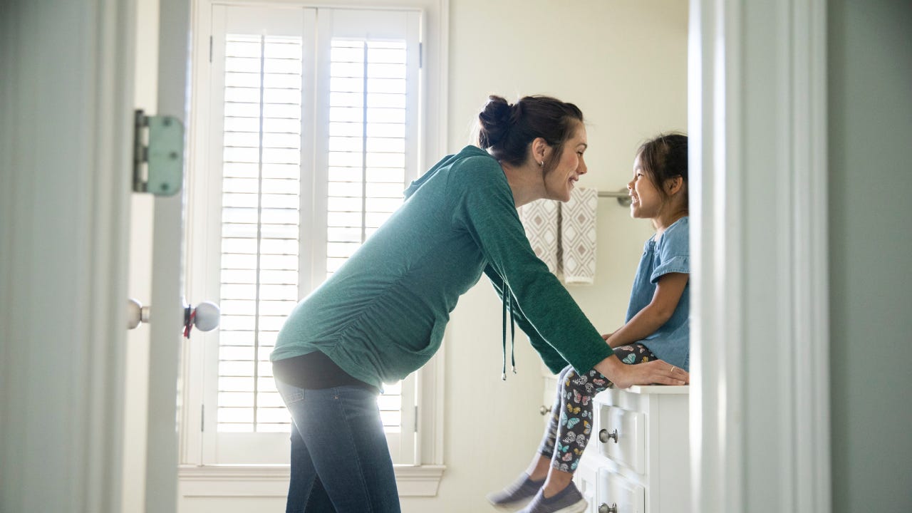 Mother talking to daughter on bathroom counter