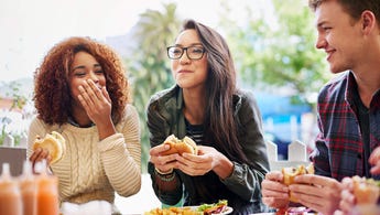 Three friends laughing and eating at an outdoor restaurant