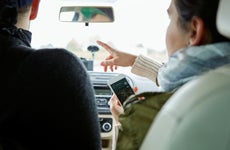 Young couple sitting in car, woman holding smartphone, pointing directions, rear view