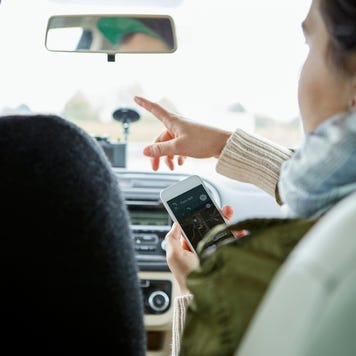 Young couple sitting in car, woman holding smartphone, pointing directions, rear view