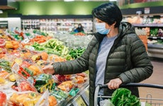 Adult woman wearing a coat and face mask shops for produce in a grocery store