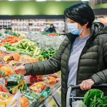 Adult woman wearing a coat and face mask shops for produce in a grocery store