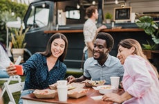 Group of friends posing for a selfie while eating food from a food truck outside