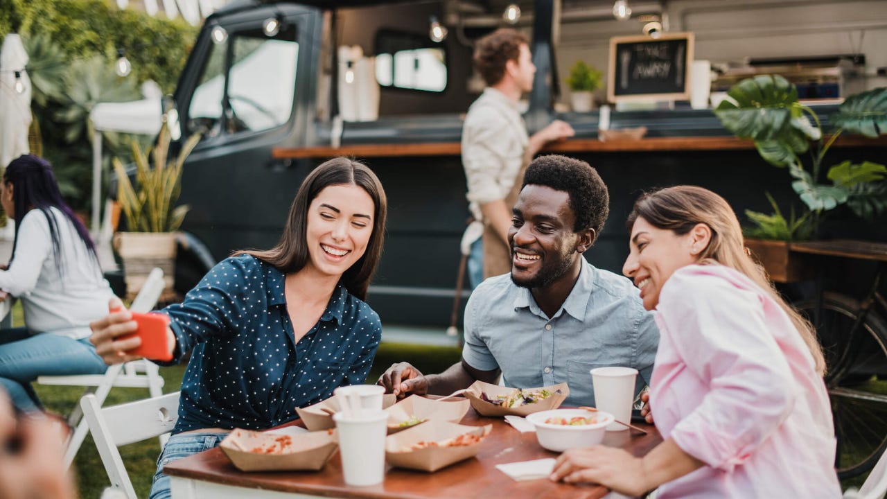 Group of friends posing for a selfie while eating food from a food truck outside