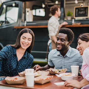 Group of friends posing for a selfie while eating food from a food truck outside