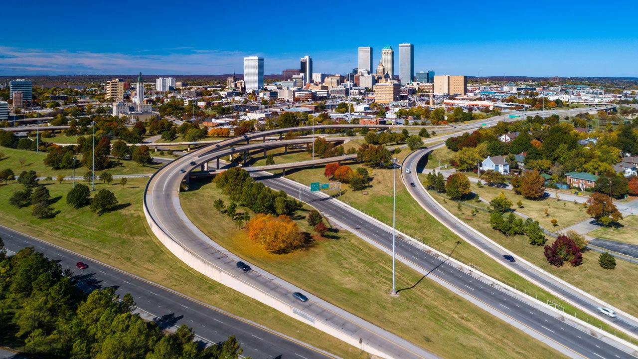 Aerial view of Downtown Tulsa skyline with grass, trees, and freeways in the foreground.