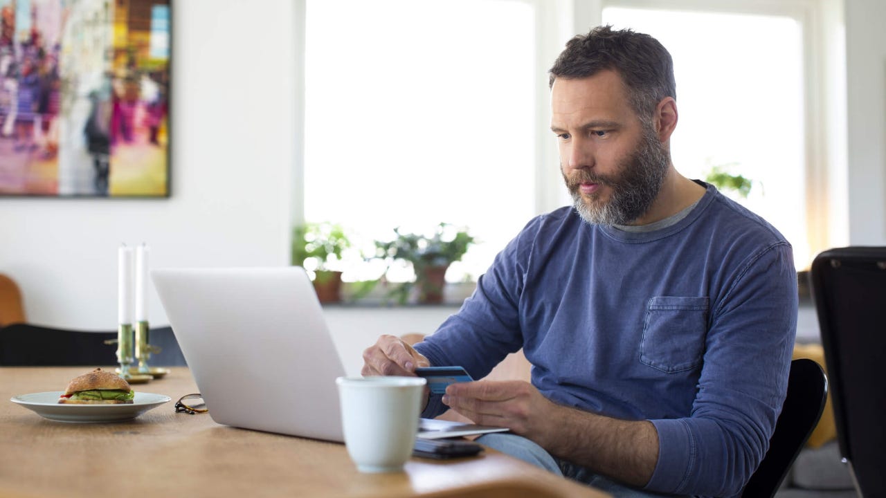 Man using laptop at home while holding credit card