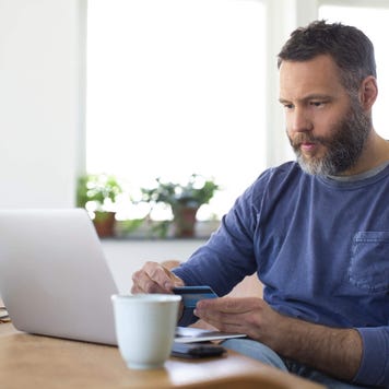 Man using laptop at home while holding credit card