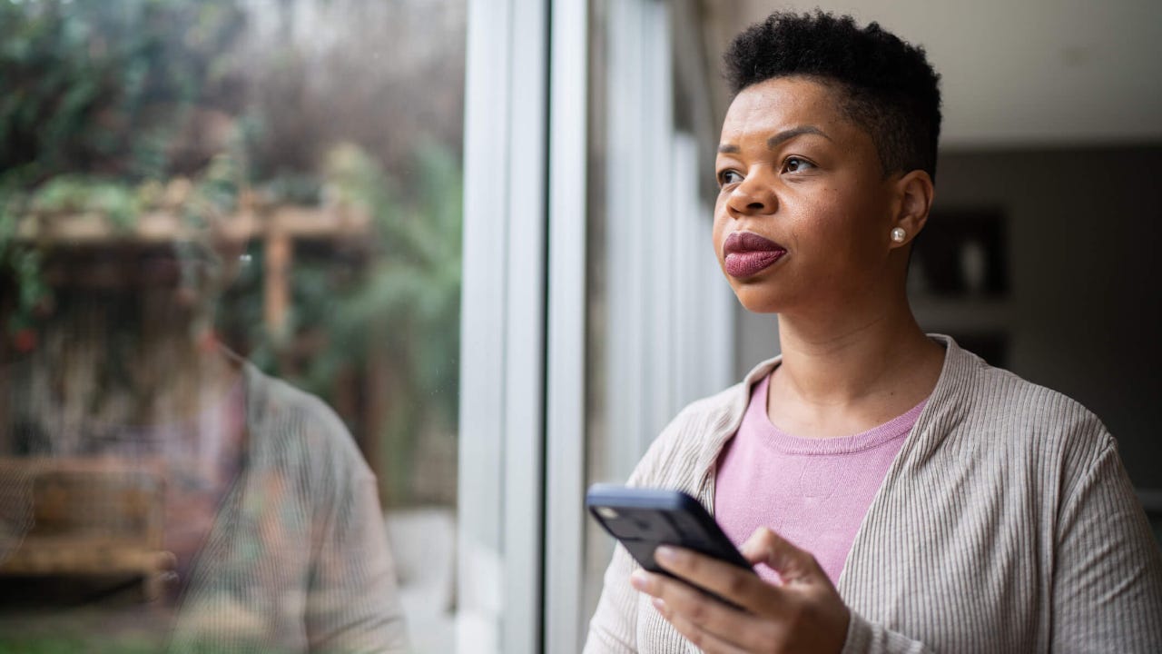 Woman contemplating and using smartphone at home