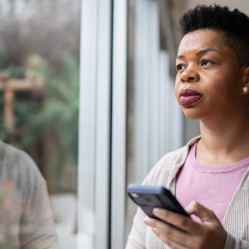 Woman contemplating and using smartphone at home