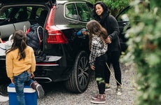 woman charging her electric car while her family packs bags into the trunk