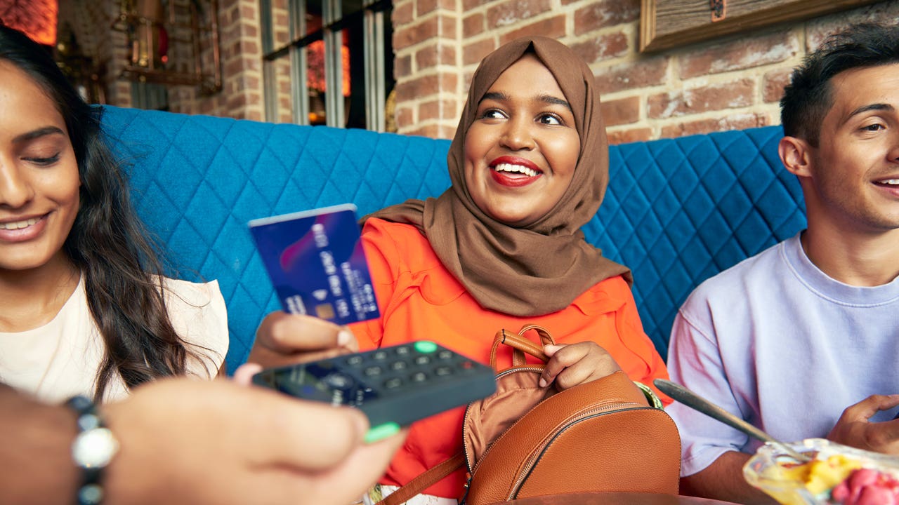 women wearing hijab hands over her credit card to pay at a restaurant