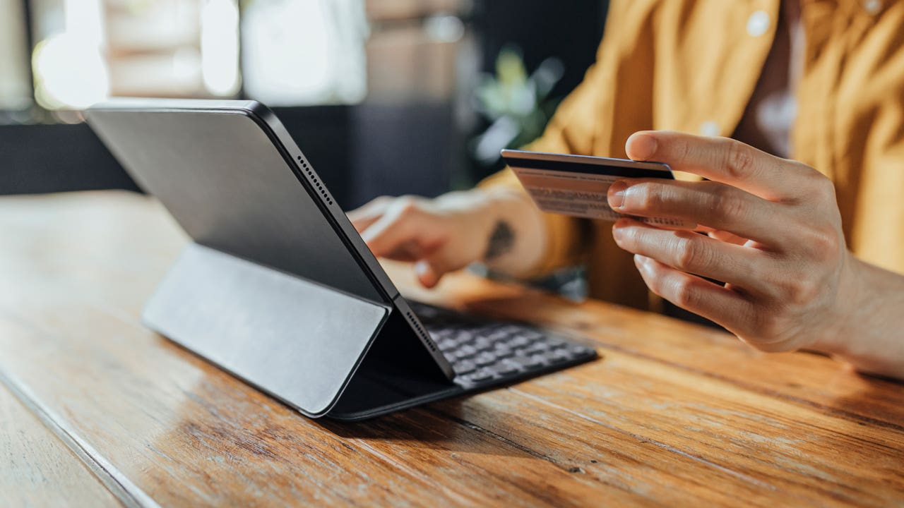 close up of hand holding credit card and typing on a digital tablet