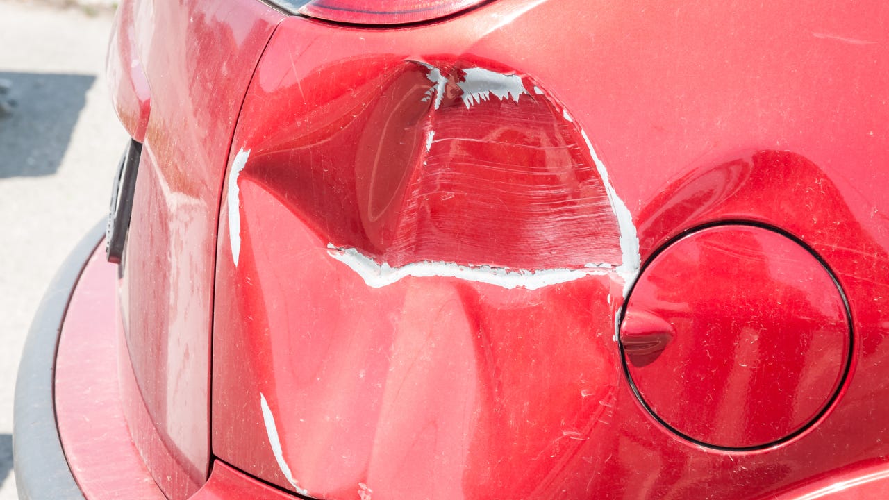 Red scratched car with damaged paint in crash accident or parking lot and dented damage of metal body from collision