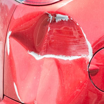 Red scratched car with damaged paint in crash accident or parking lot and dented damage of metal body from collision