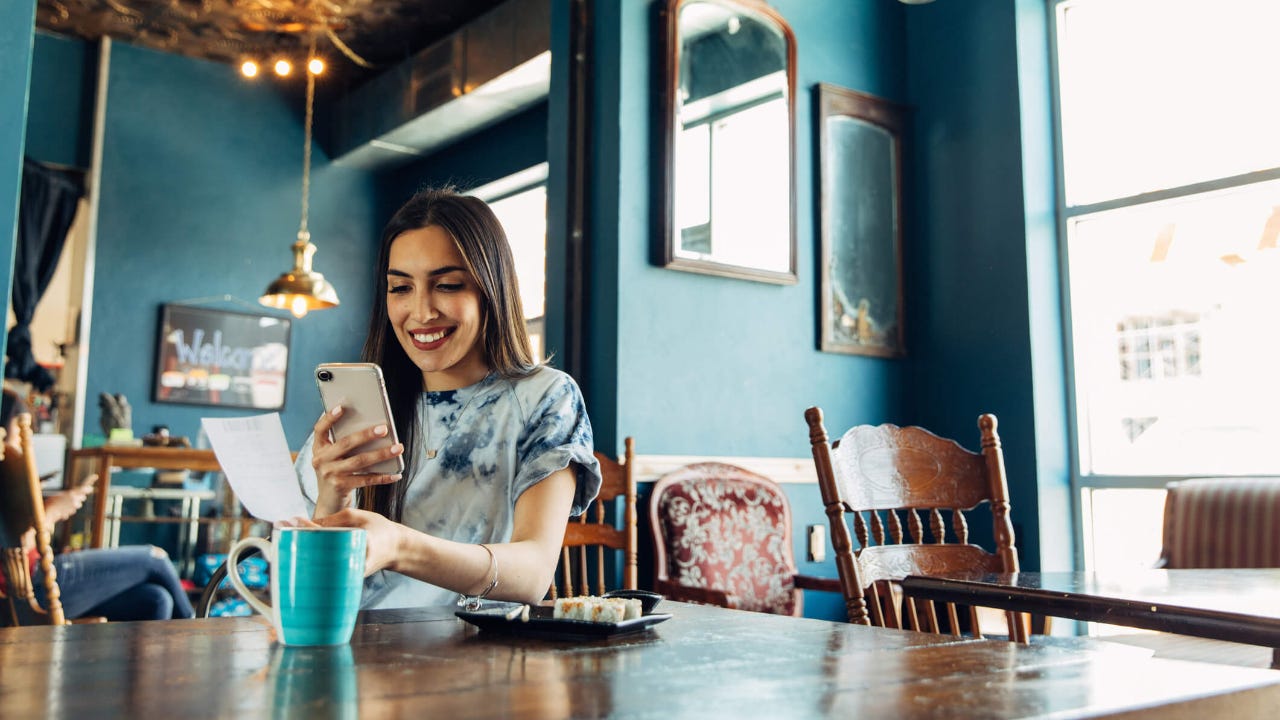 Young woman holding a receipt and her smartphone in a cafe while smiling