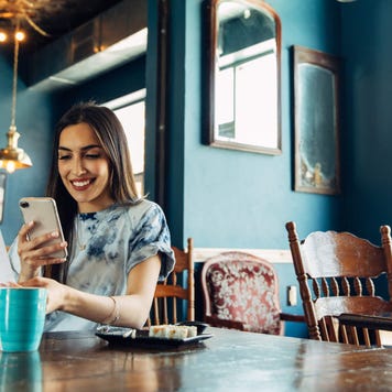 Young woman holding a receipt and her smartphone in a cafe while smiling