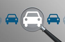 An image of five silhouetted cars, four are blue, the center is white and a magnifying glass is over it.