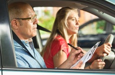A teenager young girl in the process of taking the driver examination for driver's license. She is carefully driving while the examiner is scoring her driving skill.