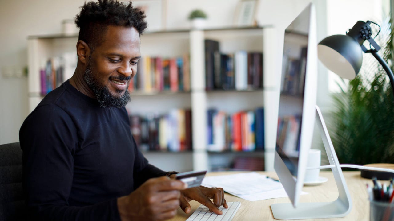 Man holding his credit card while sitting in front of desktop computer at home