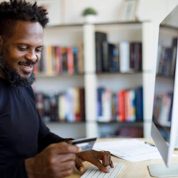 Man holding his credit card while sitting in front of desktop computer at home