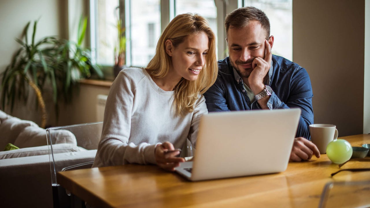 Couple sitting at kitchen table using laptop