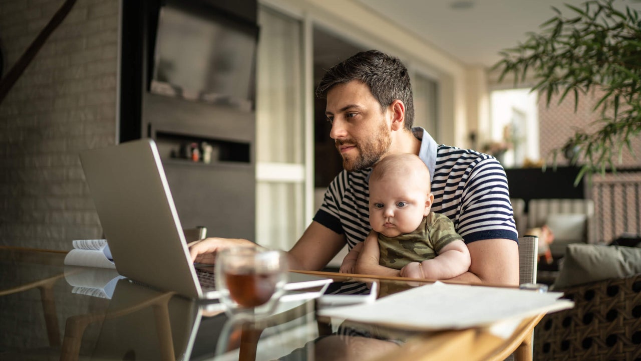 Father with baby uses laptop at kitchen table