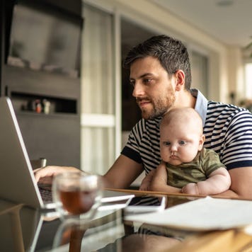 Father with baby uses laptop at kitchen table