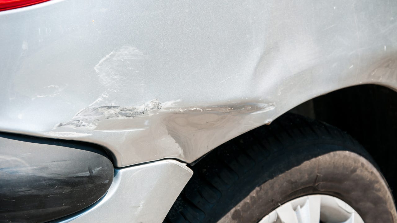 Rear side of broken and damaged silver car wreck in crash accident with scratched paint in collision close up